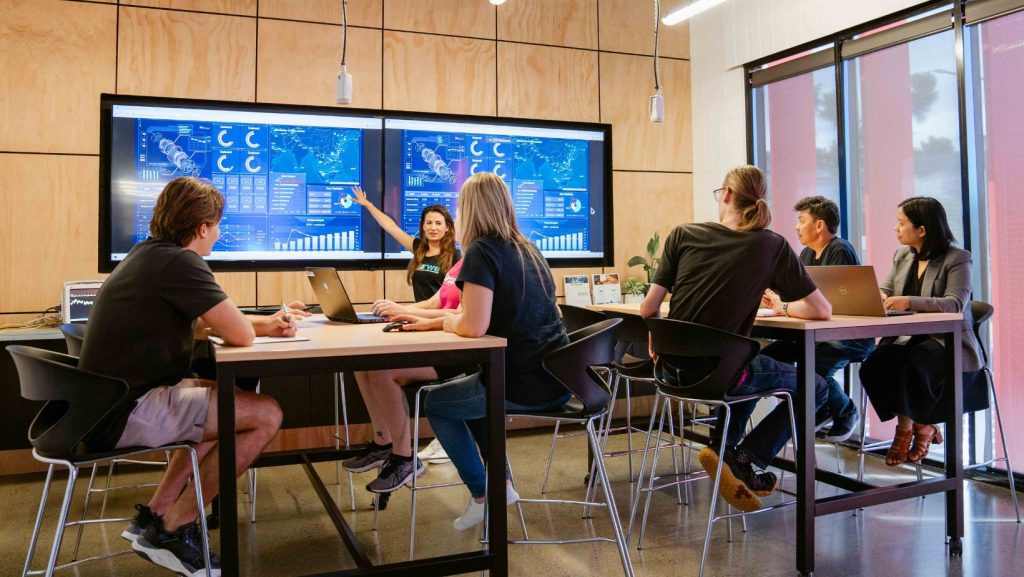 Group of people siting in a room looking at a digital screen