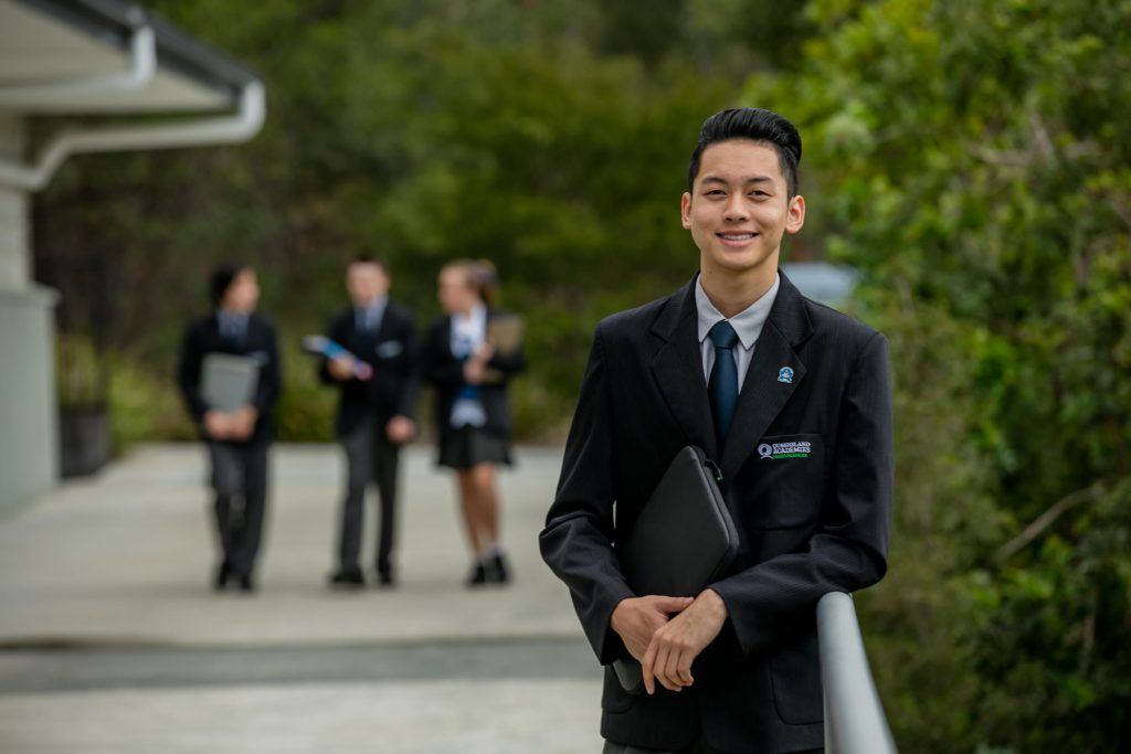 Student leaning up against a railing holding a folder
