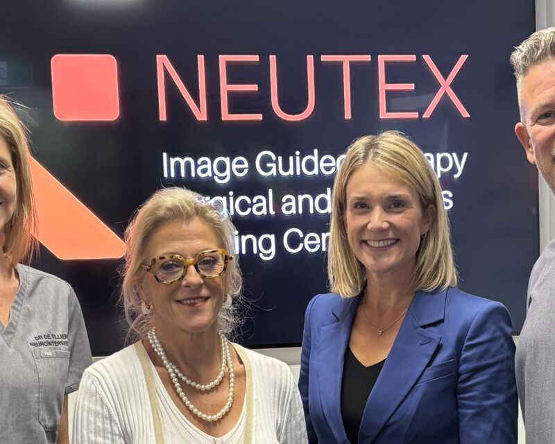 Four people stand smiling in front of a sign for NEUTEX (Image-Guided Therapy, Surgical and Robotics Training Centre). From left to right: Dr Laetitia de Villiers, Nadine Hans, Linnea Burman, and Dr Hal Rice.