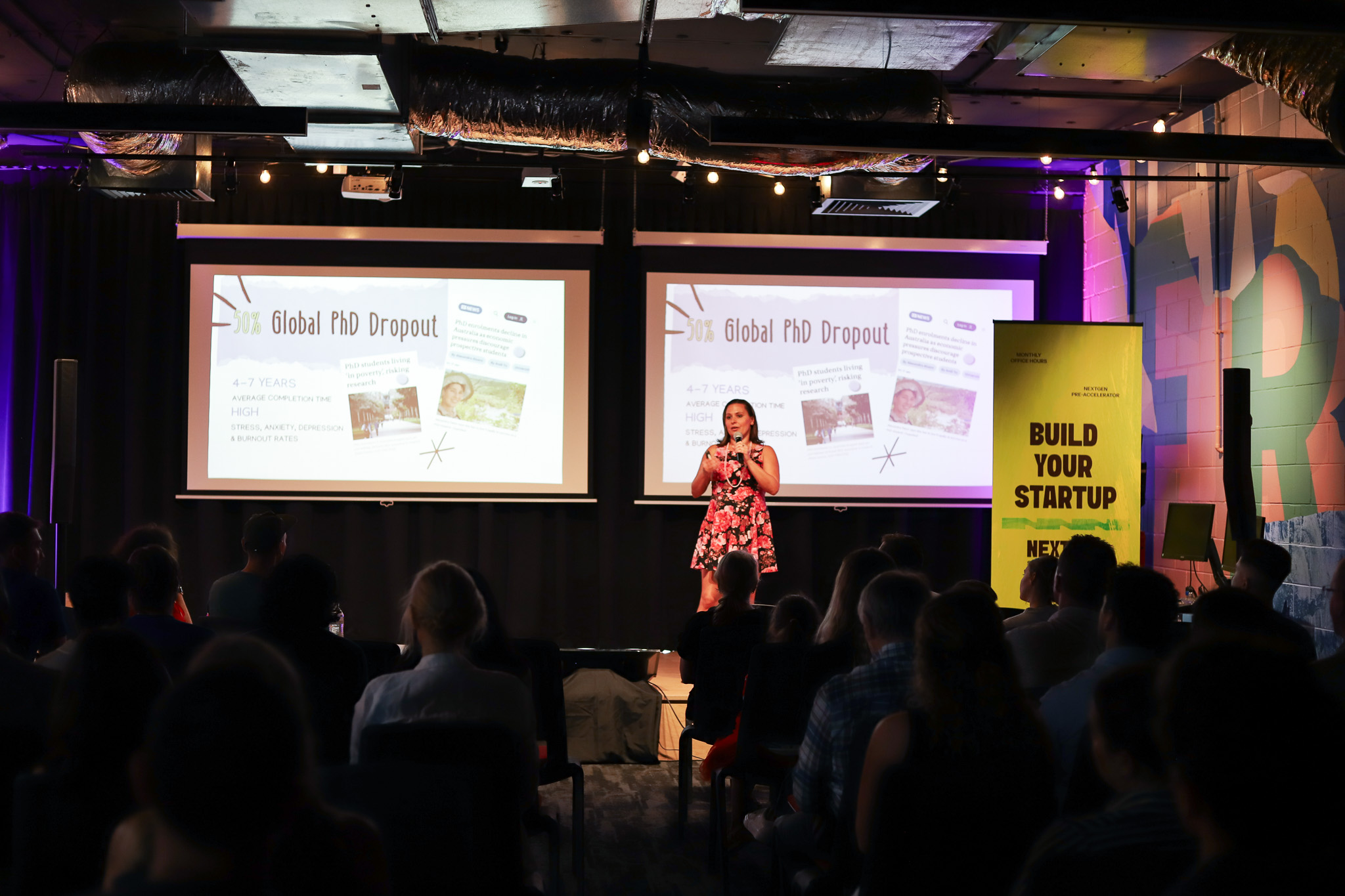 A startup founder pitches on stage in front of a projected presentation titled "50% Global PhD Dropout" during NextGen Demo Night.