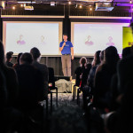 Audience watches a Cut Compass team member present on stage during the NextGen Demo Night at Cohort Innovation Space.