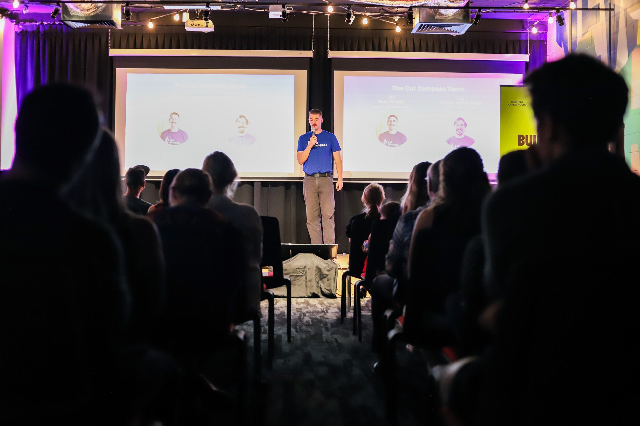 Audience watches a Cut Compass team member present on stage during the NextGen Demo Night at Cohort Innovation Space.