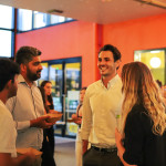 Attendees network and chat during the social portion of NextGen Demo Night, held in the brightly lit entry space at Cohort.