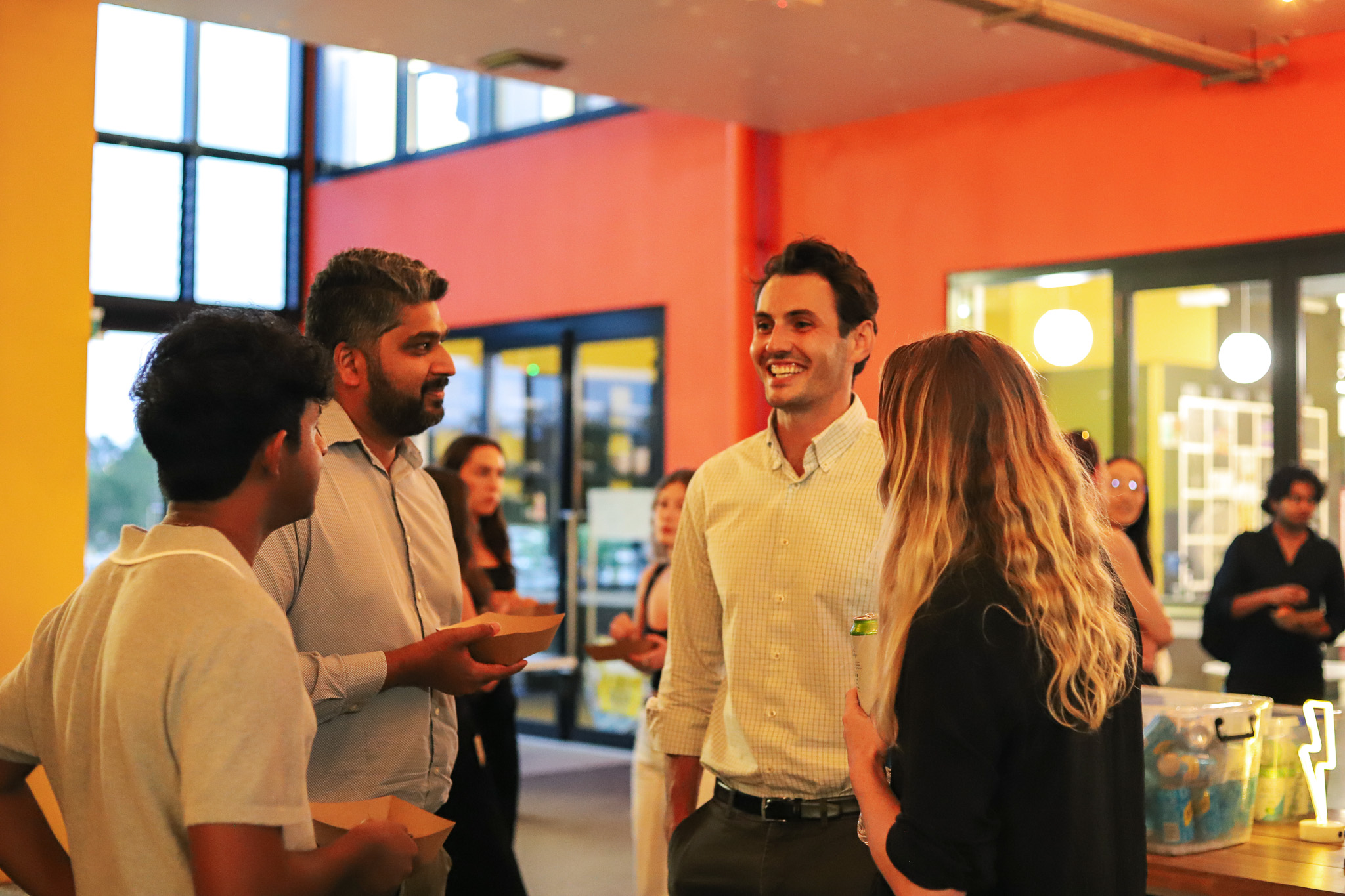 Attendees network and chat during the social portion of NextGen Demo Night, held in the brightly lit entry space at Cohort.